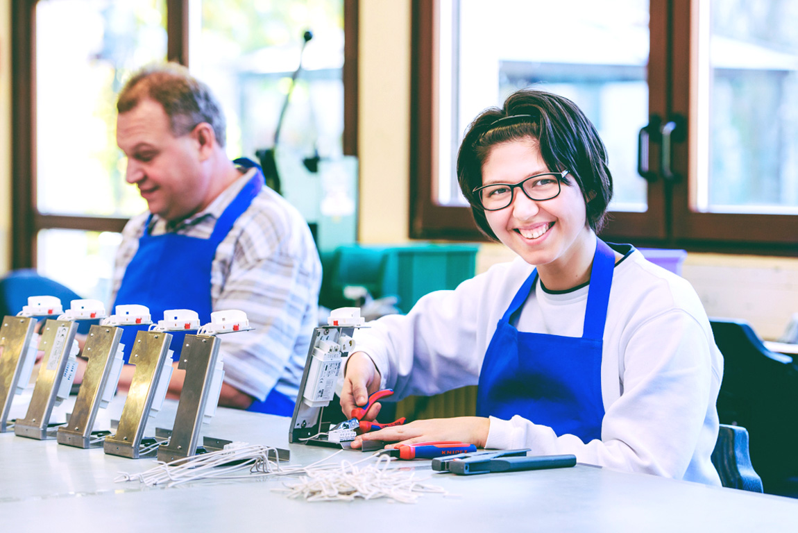 Mitarbeiterin der LebensWerkstatt verrichtet elektronische Arbeit und lächelt in die Kamera.