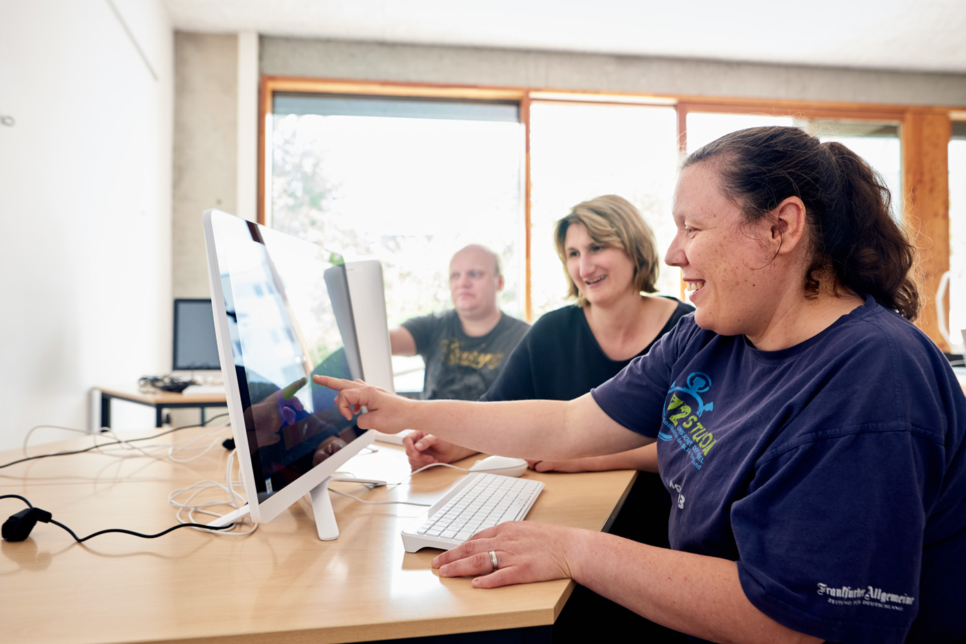 Frau unterstützt zwei Menschen mit Behinderung bei der Arbeit am Computer