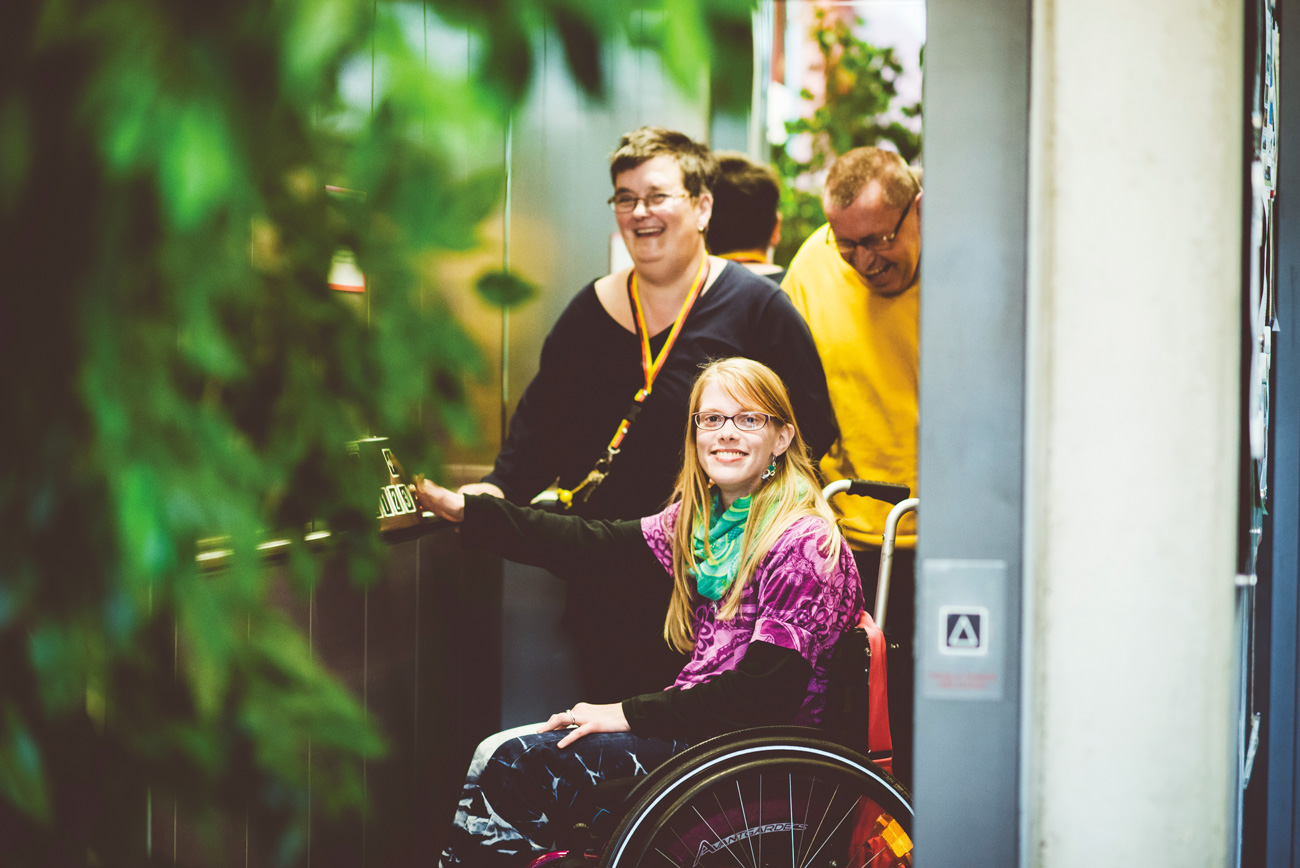 Eine Frau im Rollstuhl fährt mit zwei weiteren Bewohnern Aufzug