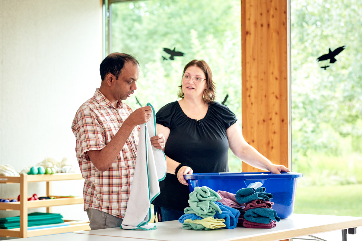 Einem Bewohner der LebensWerkstatt wird beim Wäschezusammenlegen geholfen.