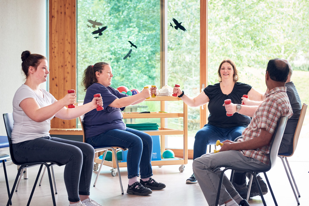 In einem Sitzkreis machen Bewohner sportliche Übungen mit Hanteln.