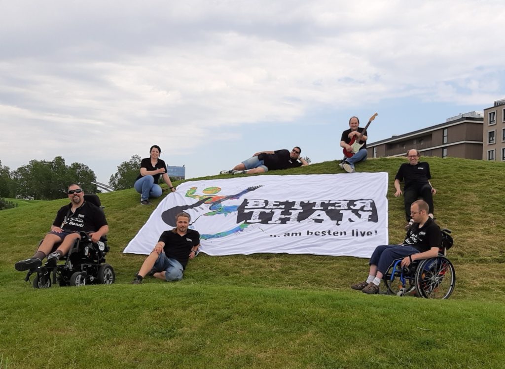 Bandmitglieder posieren auf einem Hügel mit einem Better Than ... am besten live! Banner. Entspannt und fröhlich.