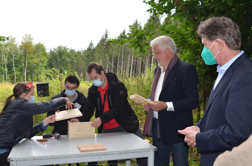 Gruppe von Menschen baut Vogelhaus im Freien, alle tragen Masken und stehen an einem Tisch.