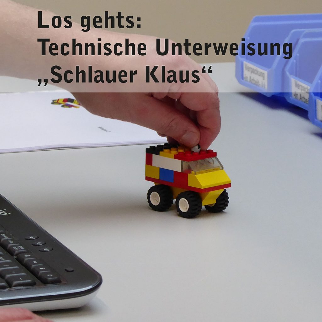 Person hält Lego-Auto am Schreibtisch mit der Aufschrift Technische Unterweisung: Schlauer Klaus.