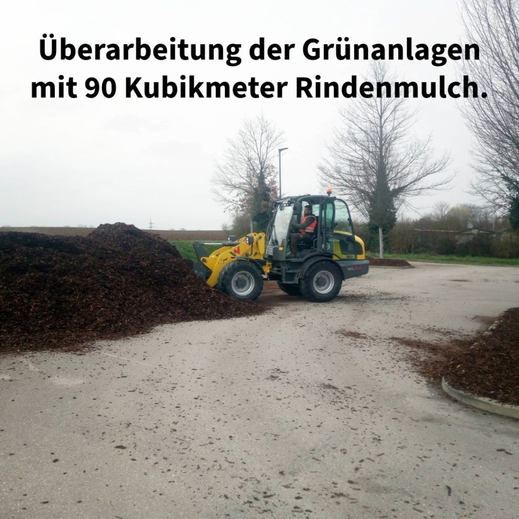 Bagger verteilt Rindenmulch auf großer Fläche zur Grünanlagenpflege.