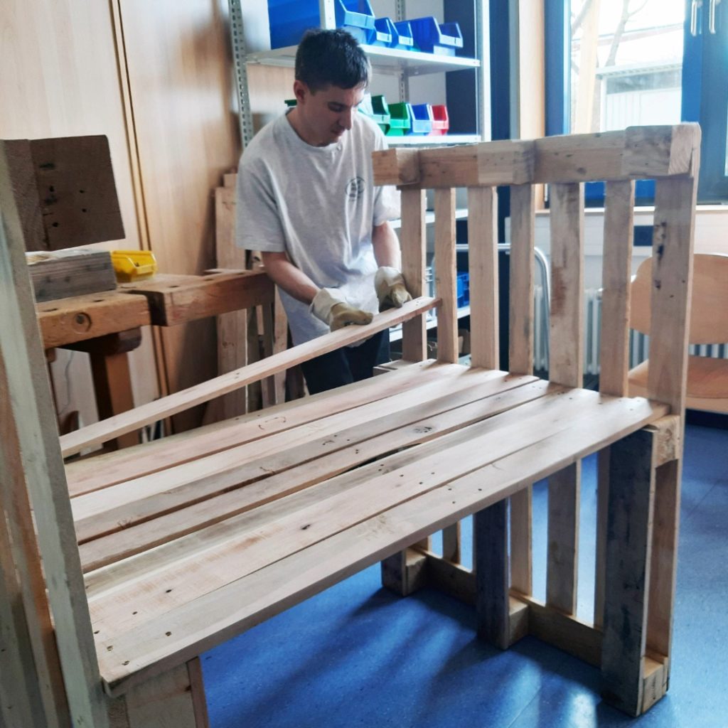 Person baut Bank aus Holzpaletten in Werkstatt.
