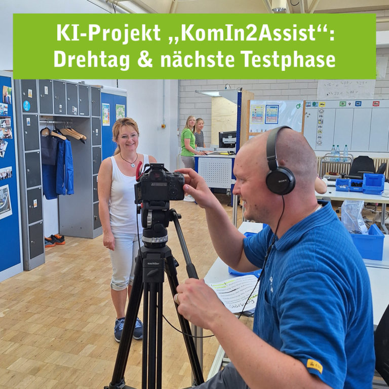 Eine Frau steht vor der Kamera und lächelt, während ein Mann mit Kopfhörern die Kamera bedient. Im Hintergrund sind Arbeitsplätze und Schließfächer zu sehen. Der Text 'KI-Projekt KomIn2Assist: Drehtag & nächste Testphase' ist oben im Bild eingeblendet.