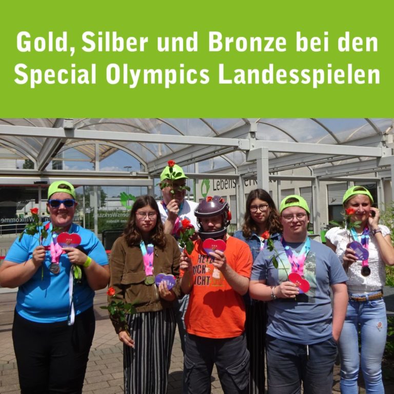 Sieben Sportlerinnen und Sportler stehen vor einem Gebäude, tragen Medaillen und halten Blumen. Sie freuen sich über ihren Erfolg bei den Special Olympics Landesspielen.