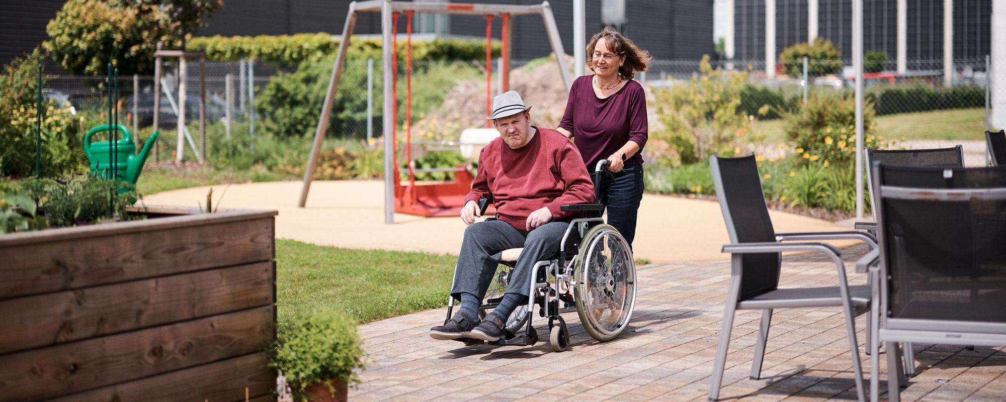 eine frau schiebt einen mann im rollstuhl durch einen garten