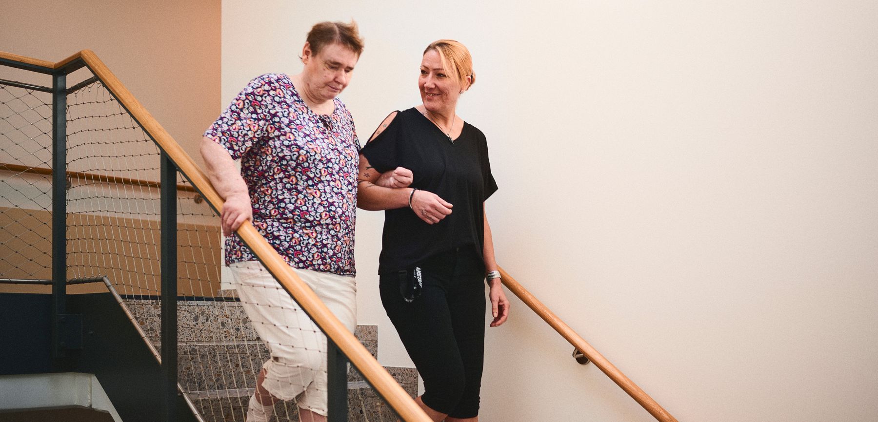 Ältere Frau wird beim Treppensteigen von einer Pflegekraft unterstützt. Pflege und Unterstützung im Alltag.