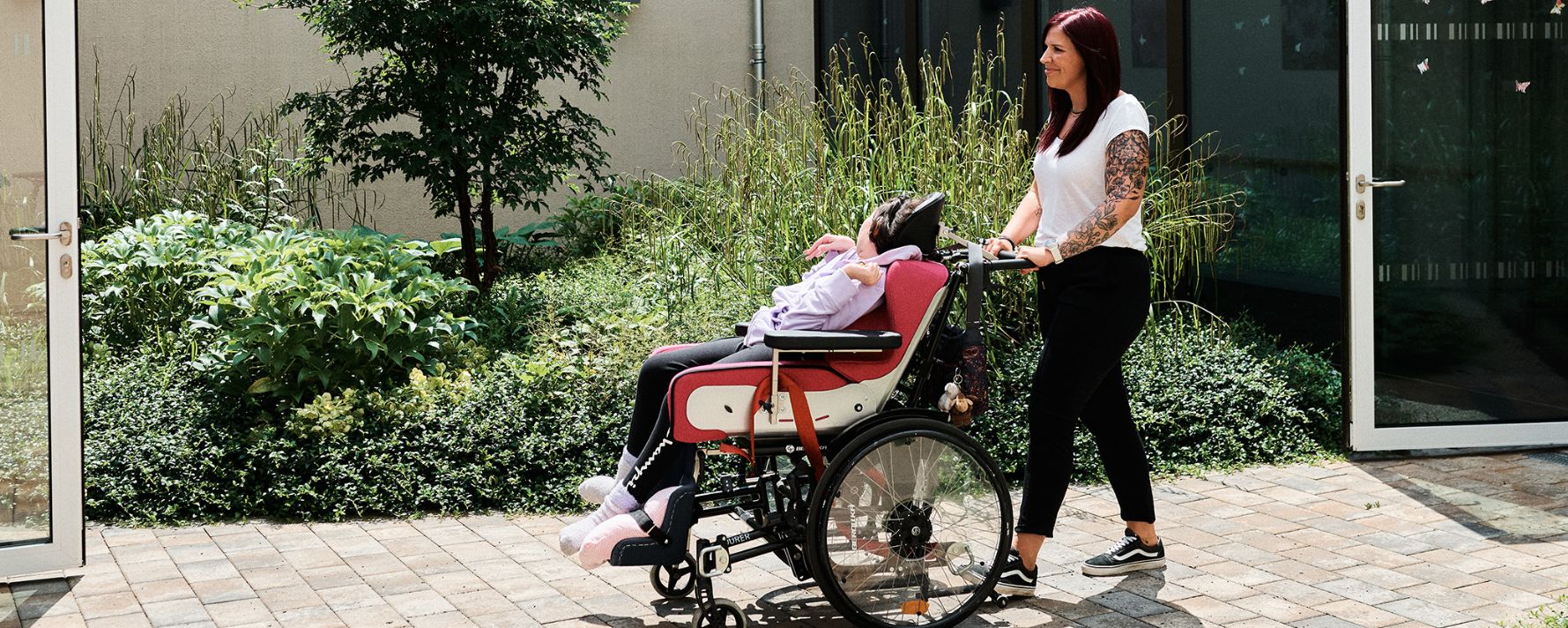 Eine Frau schiebt einen Menschen im Rollstuhl