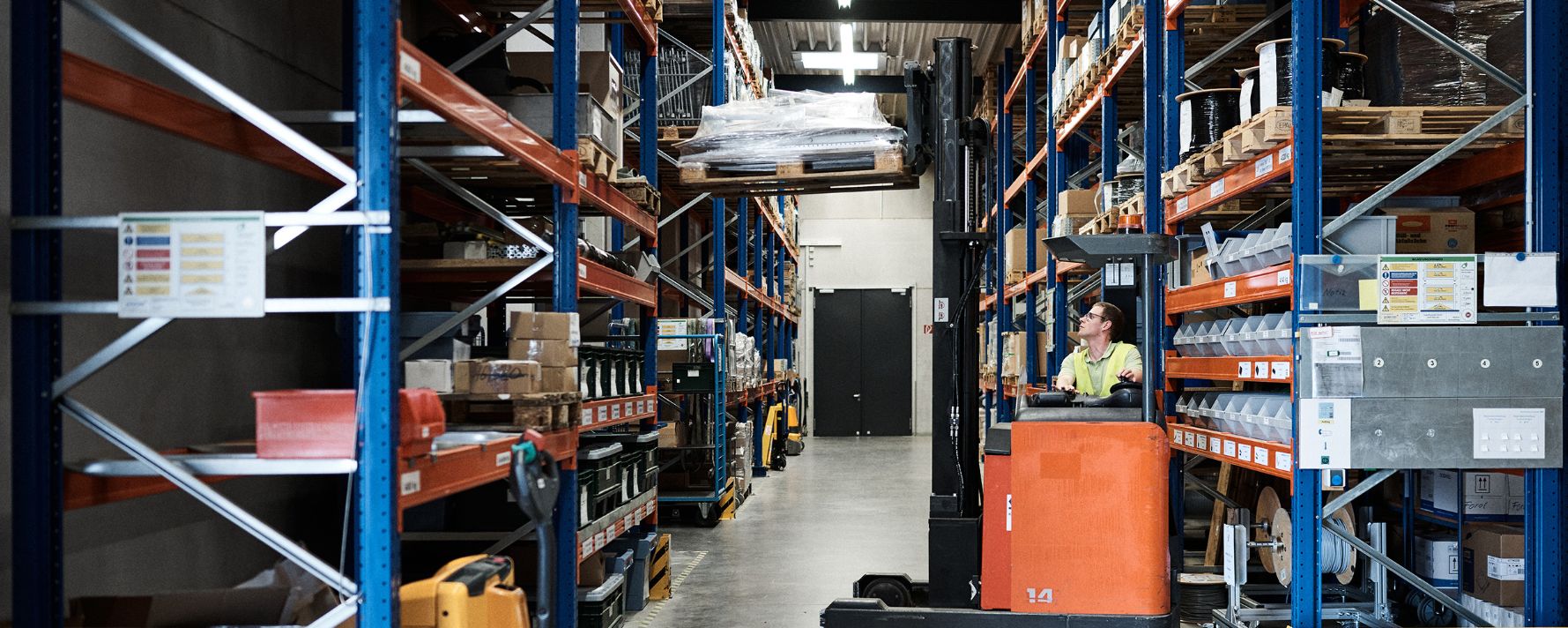Blick in ein aufgeräumtes, ordentliches Lager in dem ein Mann einen Gabelstapler fährt