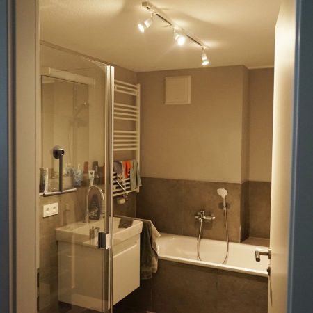 Modernes Badezimmer mit Dusche, Badewanne und Handtuchheizkörper. Helle Beleuchtung und einfache Gestaltung.