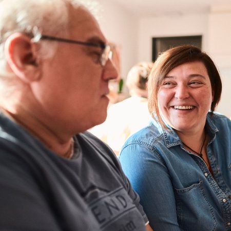 Lächelnde Frau und nachdenklicher Mann sitzen zusammen und unterhalten sich in einem hellen Raum.