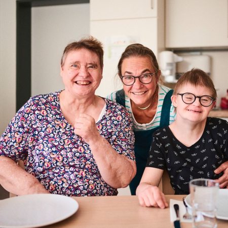 drei menschen lachen in die kamera und sitzen an einem küchentisch