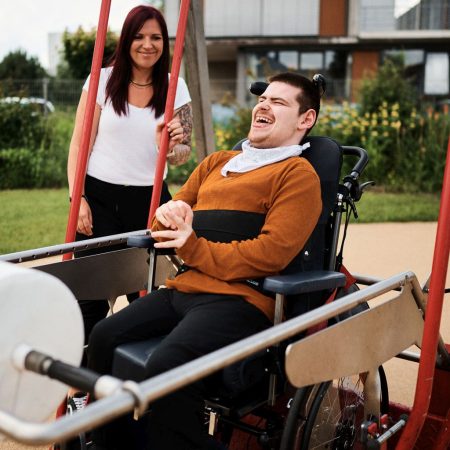 eine frau steht neben einem mann im rollstuhl der in einer großen rollstuhlschaukel ist