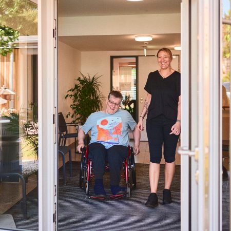 eine frau im rollstuhl sitzt neben einer betreuerin - beide schauen auf eine terrasse