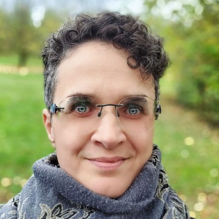 Ulrike Richter mit lockigem Haar und Schal lächelt im Park.